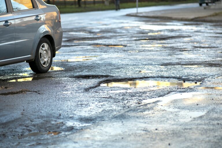 Close up of car wheel on a road in very bad condition with big potholes full of dirty rain water